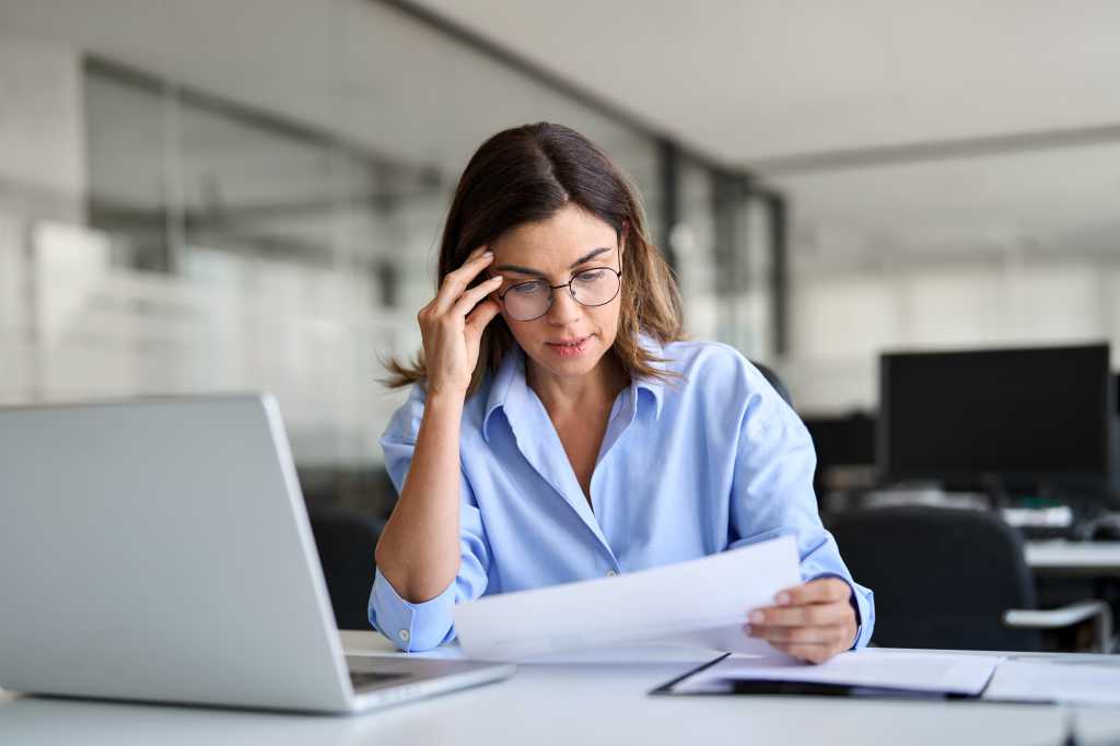 Worried mature professional business woman reading bad news in document at work. Tired upset busy 40s middle aged businesswoman feeling stress looking at paper bill having problem in office.