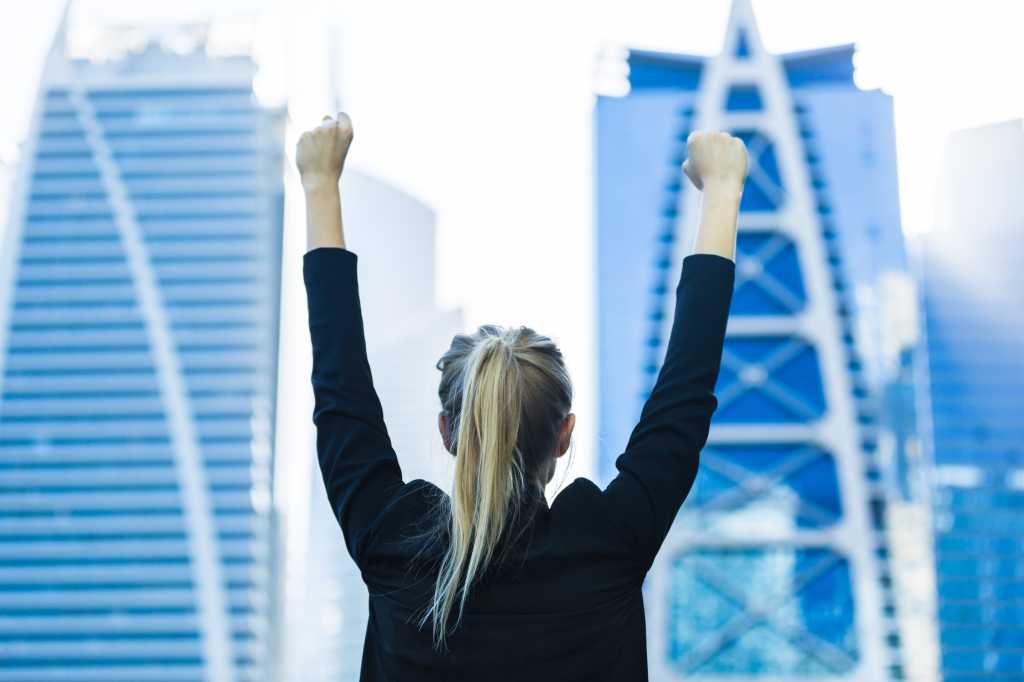 Business success - Celebrating businesswoman overlooking the city center high-rises.