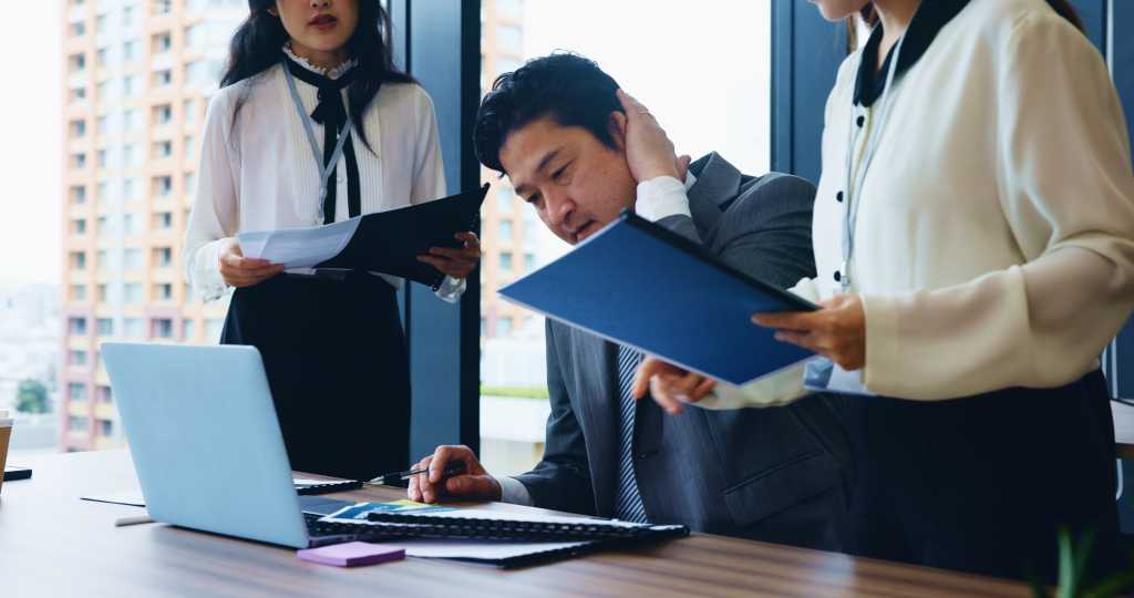 Laptop, stress and business people with planning, man and accounting with research for stock market. Employees, time management and leader with documents, pressure and multitasking in Japan